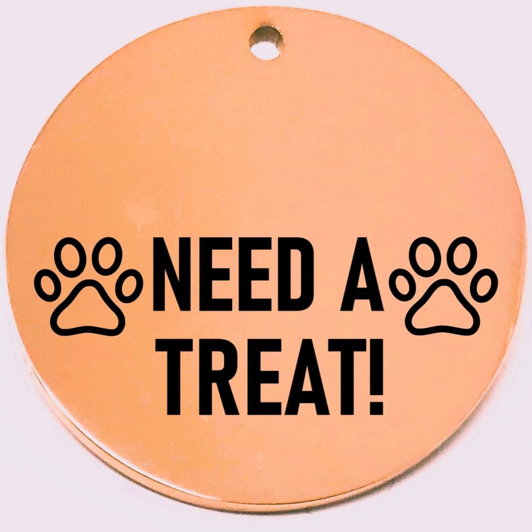 Round rose gold pet tag with black text 'NEED A TREAT!' and paw prints on a white background