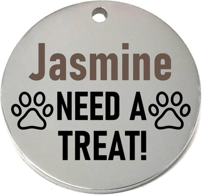 Round silver pet id tag with 'Jasmine NEED A TREAT!' text and paw prints on a white background